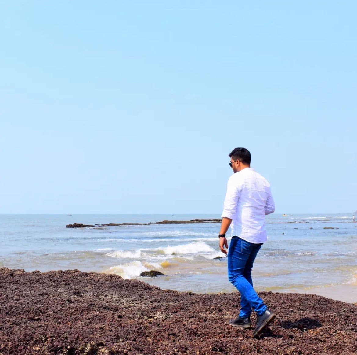 Manas Majhi walking along the rocky Goa coastline in a white shirt