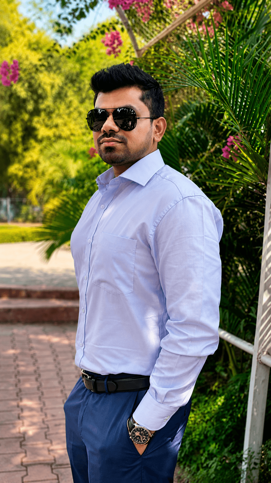 Manas Majhi in a white shirt and aviators, outdoor garden with pink bougainvillea