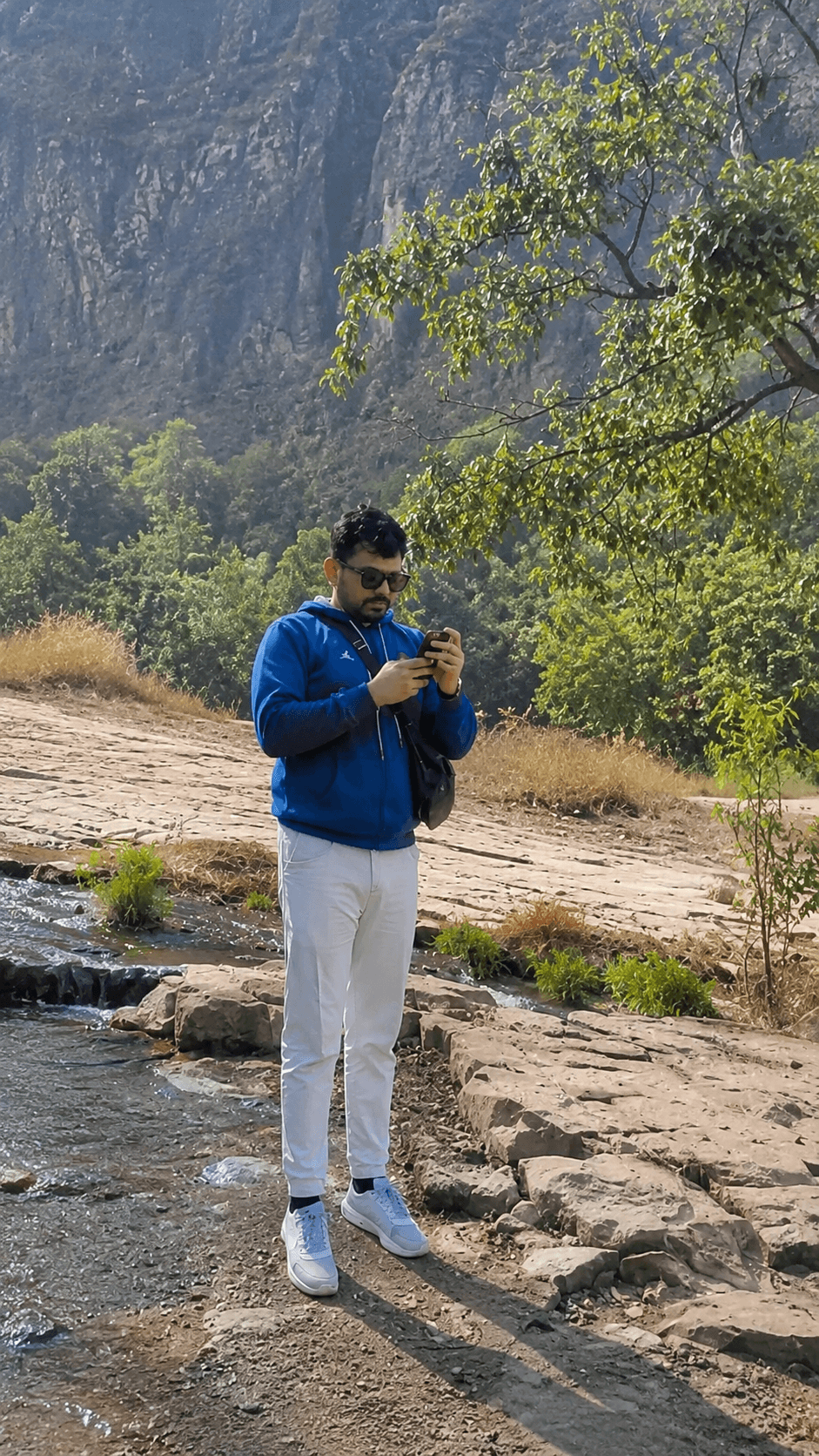 Manas Majhi standing on a rocky hillside, checking his phone